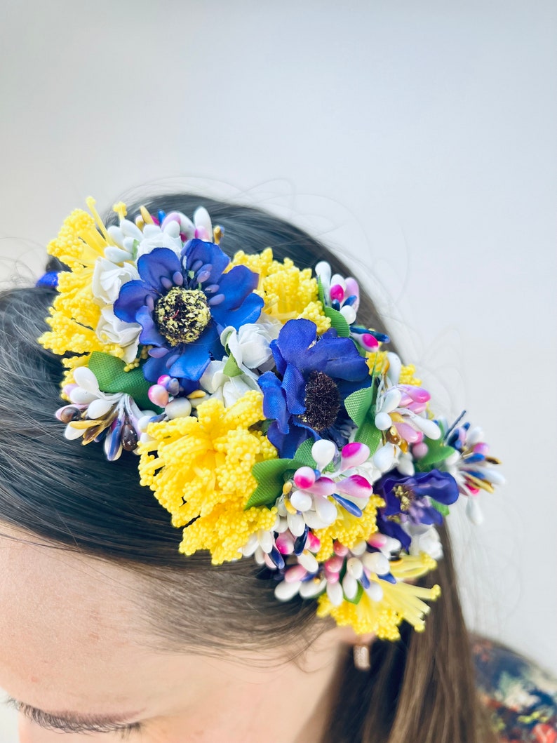 May include: A headband with yellow, blue, and white fabric flowers. The flowers are arranged in a cluster and are attached to a black headband.