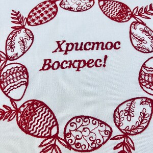 May include: Embroidered white fabric with a red wreath of stylized Easter eggs and the text "Хриcтоc Воскрес!" which translates to "Christ is Risen!" in English.