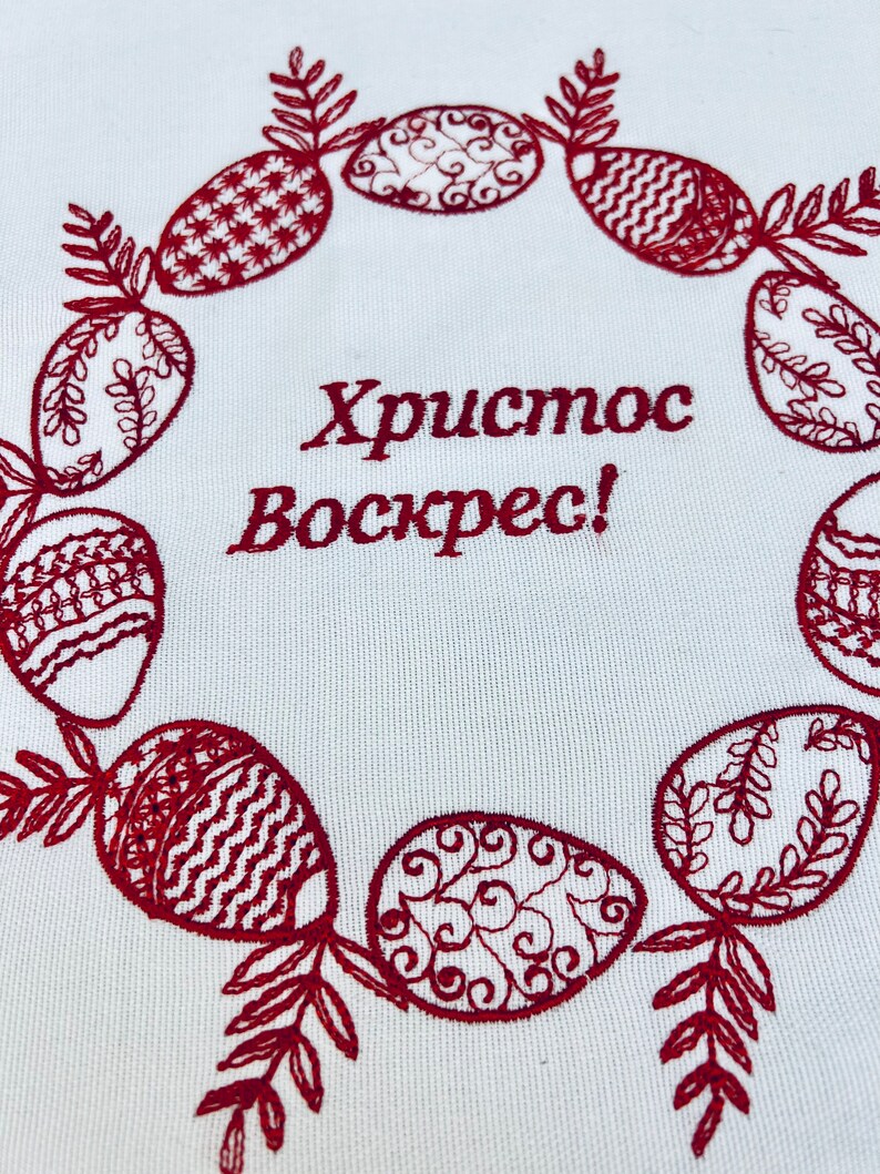 May include: Embroidered white fabric with a red wreath of stylized Easter eggs and the text "Хриcтоc Воскрес!" which translates to "Christ is Risen!" in English.