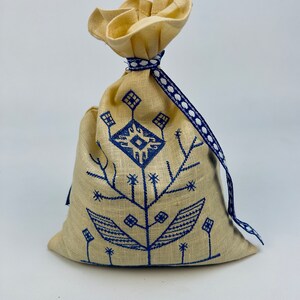 K&ouml;nnte beinhalten: Eine kleine, cremefarbene Stofftasche mit einem blau-wei&szlig;en Band. Die Tasche ist mit einem blauen, gestickten Blumenmuster verziert.