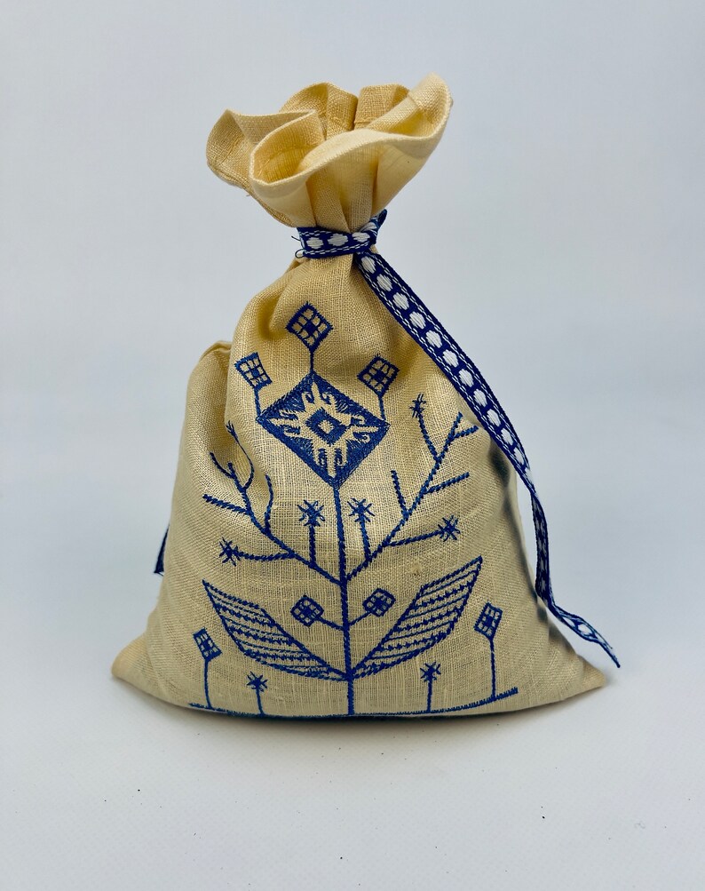 K&ouml;nnte beinhalten: Eine kleine, cremefarbene Stofftasche mit einem blau-wei&szlig;en Band. Die Tasche ist mit einem blauen, gestickten Blumenmuster verziert.
