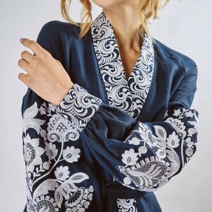 May include: A navy blue dress with white embroidered floral patterns on the sleeves and collar. The dress has a long sleeve and a V-neck.