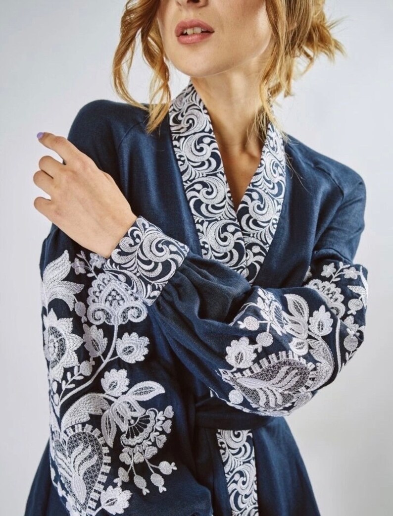 May include: A navy blue dress with white embroidered floral patterns on the sleeves and collar. The dress has a long sleeve and a V-neck.