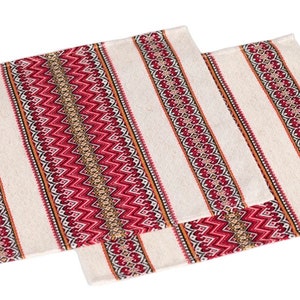 Op de afbeelding: Twee rechthoekige cr&egrave;mekleurige placemats met een streepjespatroon. Elke placemat heeft een centrale band van rode en gouden zigzags, omzoomd door rode en bruine decoratieve patronen. Het ontwerp wordt herhaald op de kleinere placemat.