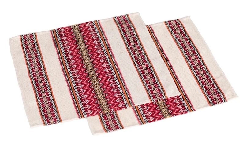Op de afbeelding: Twee rechthoekige cr&egrave;mekleurige placemats met een streepjespatroon. Elke placemat heeft een centrale band van rode en gouden zigzags, omzoomd door rode en bruine decoratieve patronen. Het ontwerp wordt herhaald op de kleinere placemat.