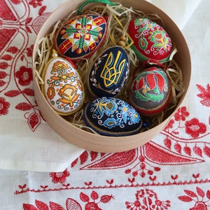 K&ouml;nnte beinhalten: Sechs bestickte Ostereier in einer Holzkiste mit Stroh. Die Eier sind mit traditionellen ukrainischen Volksmotiven verziert, darunter Blumen, geometrische Muster und der ukrainische Dreizack.