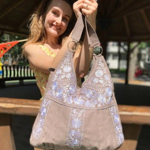 Peut inclure: Un sac cabas en toile marron avec des motifs floraux brod&eacute;s blancs et bleu clair. Le sac a deux anses et une fermeture &eacute;clair sup&eacute;rieure.