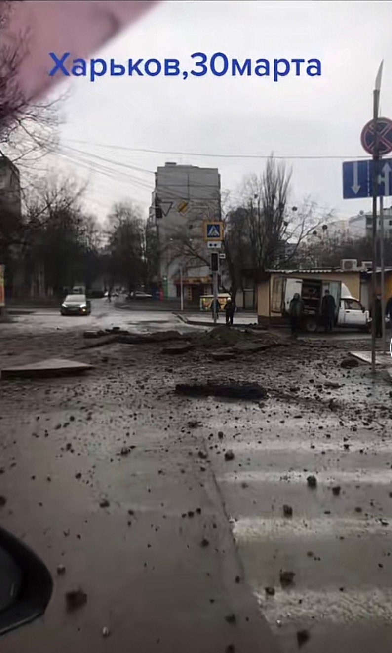 K&ouml;nnte beinhalten: Eine Stra&szlig;enszene in Charkiw, Ukraine, mit dem Datum 30. M&auml;rz im Himmel. Die Stra&szlig;e ist besch&auml;digt, mit Tr&uuml;mmern auf dem nassen Asphalt. Geb&auml;ude und B&auml;ume s&auml;umen die Stra&szlig;e.