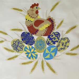 Pu&ograve; includere: Disegno ricamato di una gallina marrone e gialla circondata da spighe di grano e uova colorate con motivi blu, gialli e bianchi.