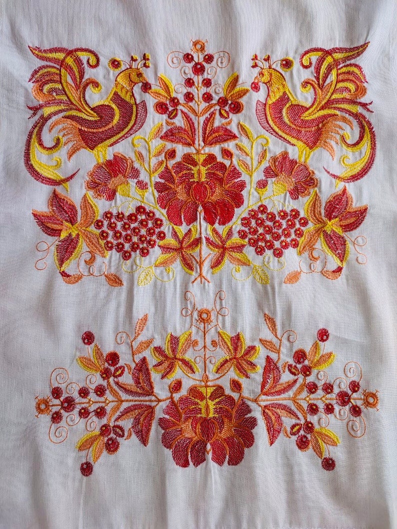 May include: White fabric with embroidered red, yellow, and orange floral design. The design features two stylized birds with long tails and a central floral motif.