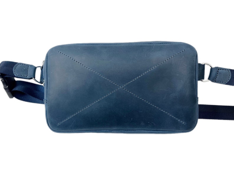May include: A dark blue leather crossbody bag with a flap closure and adjustable strap. The bag has a stitched X pattern on the front.