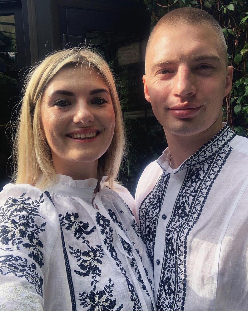 Puede incluir: Un selfie de dos personas que visten camisas blancas con intrincados bordados negros. Las camisas presentan detallados dise&ntilde;os florales y geom&eacute;tricos alrededor del cuello, las mangas y el pecho. La mujer tiene el pelo rubio y el hombre tiene el pelo corto.