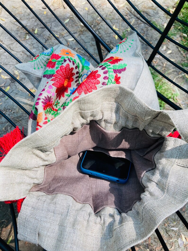 May include: A gray linen tote bag with a floral embroidered design. The bag is open and a blue smartphone is inside.