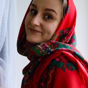 Puede incluir: Una mujer con un pa&ntilde;uelo rojo con estampado floral. El pa&ntilde;uelo est&aacute; atado debajo de la barbilla y cubre su cabello. Ella est&aacute; mirando a la c&aacute;mara y sonriendo.