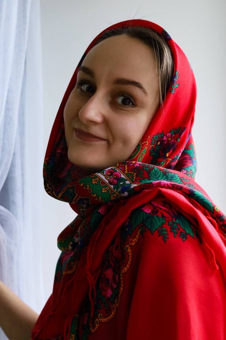 Puede incluir: Una mujer con un pa&ntilde;uelo rojo con estampado floral. El pa&ntilde;uelo est&aacute; atado debajo de la barbilla y cubre su cabello. Ella est&aacute; mirando a la c&aacute;mara y sonriendo.