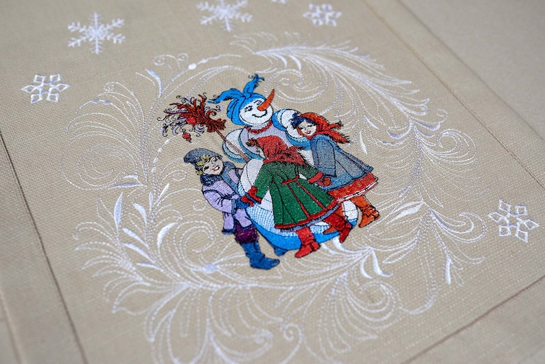 Op de afbeelding: Geborduurde wintersc&egrave;ne met een sneeuwpop en kinderen. De sneeuwpop heeft een blauwe hoed en een wortelneus. De kinderen dragen jassen in rood, groen en blauw. De achtergrond is beige met witte sneeuwvlokken en wervelpatronen.