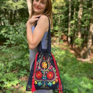 May include: A black drawstring bag with colorful floral embroidery and red tassels. The bag is made of a soft, textured fabric.