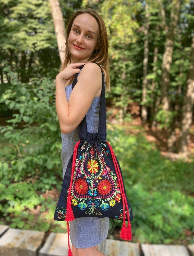 May include: A black drawstring bag with colorful floral embroidery and red tassels. The bag is made of a soft, textured fabric.