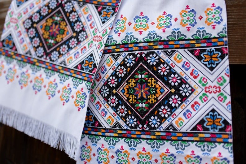 May include: White fabric with colorful embroidered floral patterns. The fabric has a fringe border.