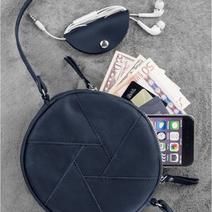 Puede incluir: Un bolso de hombro redondo de cuero azul oscuro con un patr&oacute;n geom&eacute;trico. El bolso tiene un cierre de cremallera y una correa larga ajustable. El bolso se muestra con un tel&eacute;fono, dinero en efectivo y una tarjeta en su interior.