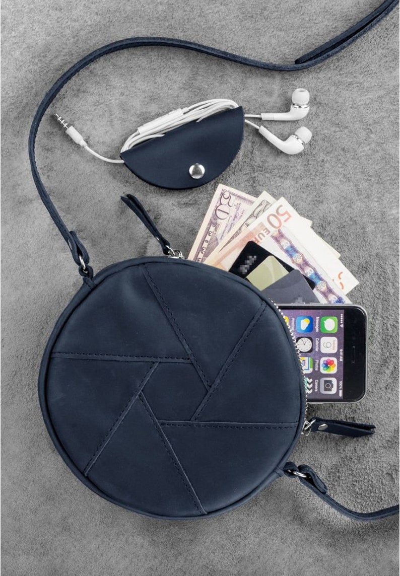 Puede incluir: Un bolso de hombro redondo de cuero azul oscuro con un patr&oacute;n geom&eacute;trico. El bolso tiene un cierre de cremallera y una correa larga ajustable. El bolso se muestra con un tel&eacute;fono, dinero en efectivo y una tarjeta en su interior.