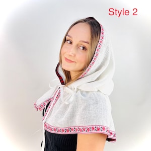 May include: White linen hooded cape with a red and black plaid lining and a floral embroidered trim. The cape has a white ribbon tie. Style 2.