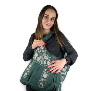 K&ouml;nnte beinhalten: Dunkelgr&uuml;ne Schultertasche mit aufwendiger wei&szlig;er Blumenstickerei. Die Tasche hat eine abgerundete Form und einen breiten Riemen. Die Stickerei ist detailliert und bedeckt die Oberseite und die Vorderseite der Tasche.