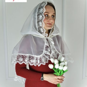 Puede incluir: Un velo blanco con capucha y ribete de encaje floral. El velo se lleva sobre un vestido rojo de manga larga. El texto "Style 1" est&aacute; en la esquina superior izquierda. La persona sostiene un ramo de tulipanes blancos.