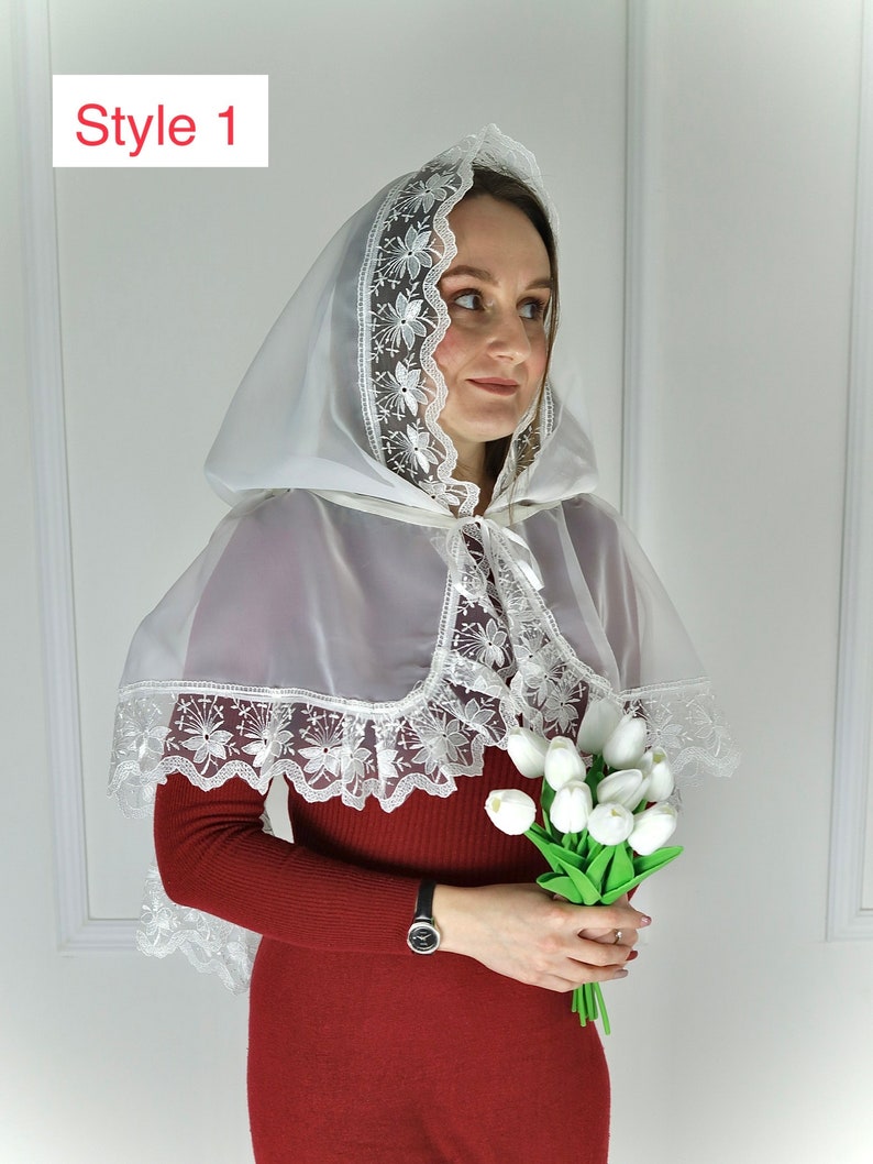 Puede incluir: Un velo blanco con capucha y ribete de encaje floral. El velo se lleva sobre un vestido rojo de manga larga. El texto "Style 1" est&aacute; en la esquina superior izquierda. La persona sostiene un ramo de tulipanes blancos.
