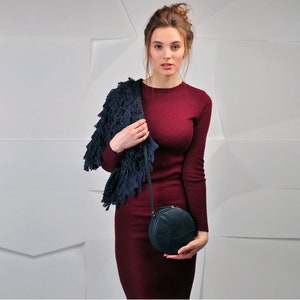 Puede incluir: Una mujer lleva un vestido granate y un c&aacute;rdigan azul con flecos y sostiene un bolso redondo de bandolera azul oscuro con un dise&ntilde;o geom&eacute;trico.