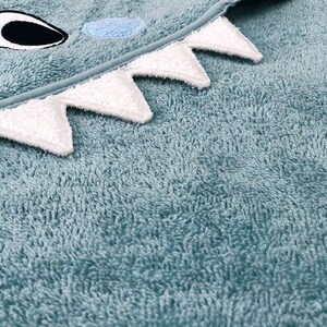 May include: A light blue hooded towel with white teeth and a black eye. The towel is made of a soft, plush material.