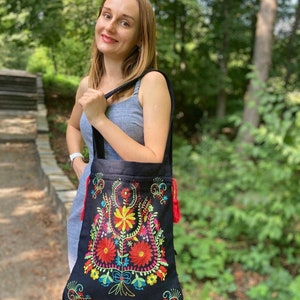 May include: A black tote bag with colorful embroidered flowers. The bag has red tassels on the sides.