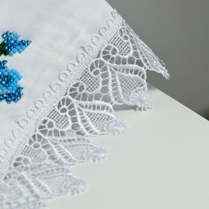 May include: White fabric with a delicate white lace trim. The lace has a scalloped edge and a floral design.