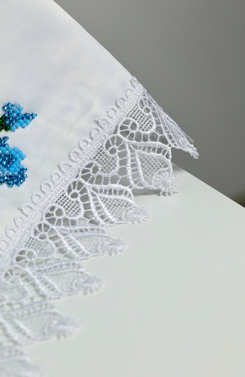 May include: White fabric with a delicate white lace trim. The lace has a scalloped edge and a floral design.
