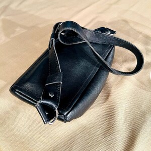 May include: A black leather crossbody bag with a long adjustable strap. The bag has a flap closure and a silver buckle.