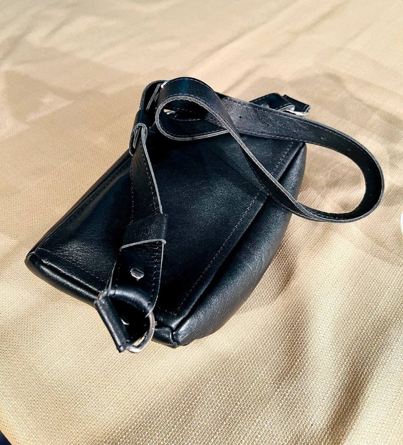 May include: A black leather crossbody bag with a long adjustable strap. The bag has a flap closure and a silver buckle.