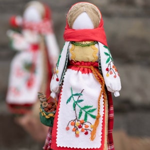 Puede incluir: Una mu&ntilde;eca de tela hecha a mano que lleva un vestido rojo y blanco con flores bordadas y un pa&ntilde;uelo rojo. La mu&ntilde;eca lleva una peque&ntilde;a cesta.