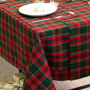 May include: A festive table setting with a red and green plaid tablecloth. The table is set with white plates, silverware, and crystal glasses. A folded napkin mirrors the tablecloth's pattern. The scene suggests a holiday or special occasion.