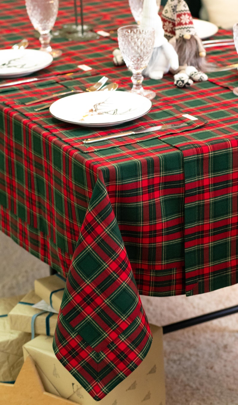 May include: A festive table setting with a red and green plaid tablecloth. The table is set with white plates, silverware, and crystal glasses. A folded napkin mirrors the tablecloth's pattern. The scene suggests a holiday or special occasion.