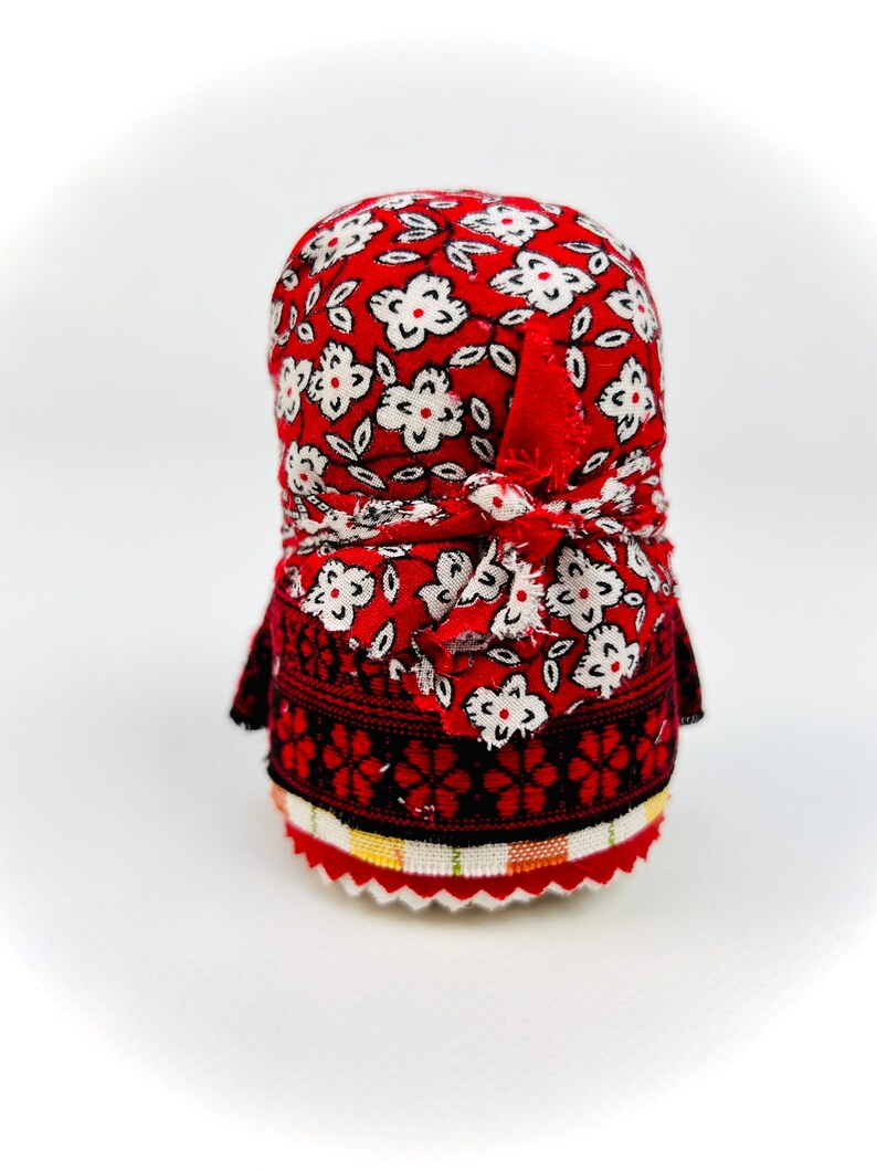 Op de afbeelding: Een traditionele Russische nestpop, of matrjosjkapop, met een rood en wit bloemenpatroon. De pop draagt een rode hoofddoek en een zwarte en rode geborduurde rok.