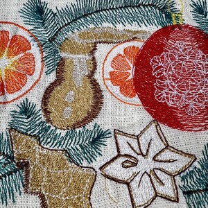 May include: Embroidered Christmas-themed design on a cream-colored fabric. Features a red ornament, orange citrus slices, a gingerbread man, a star, and green pine needles. The embroidery is in shades of gold, brown, orange, and white.