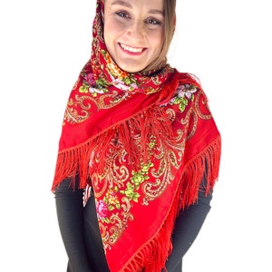 May include: A red headscarf with a floral pattern and fringe. The scarf is worn by a person with brown hair and a black shirt.