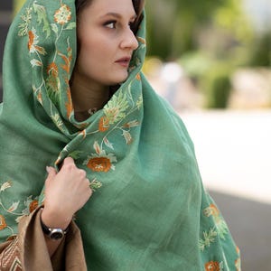 May include: A green shawl with orange and white floral embroidery. The shawl is made of a soft, lightweight fabric and is perfect for layering.