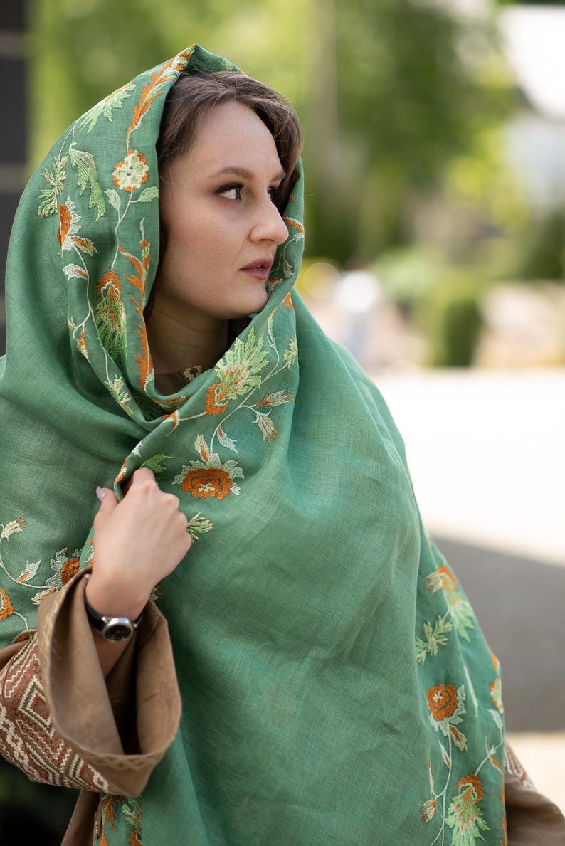 May include: A green shawl with orange and white floral embroidery. The shawl is made of a soft, lightweight fabric and is perfect for layering.