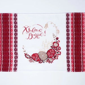 Puede incluir: Camino de mesa bordado blanco de Pascua con patrones florales y geom&eacute;tricos rojos y burdeos. El centro presenta una corona con huevos de Pascua y texto en escritura roja. Los bordes tienen flecos.