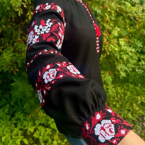 K&ouml;nnte beinhalten: Ein schwarzes Langarmhemd mit roten und wei&szlig;en gestickten Blumendesigns an den &Auml;rmeln und Manschetten.