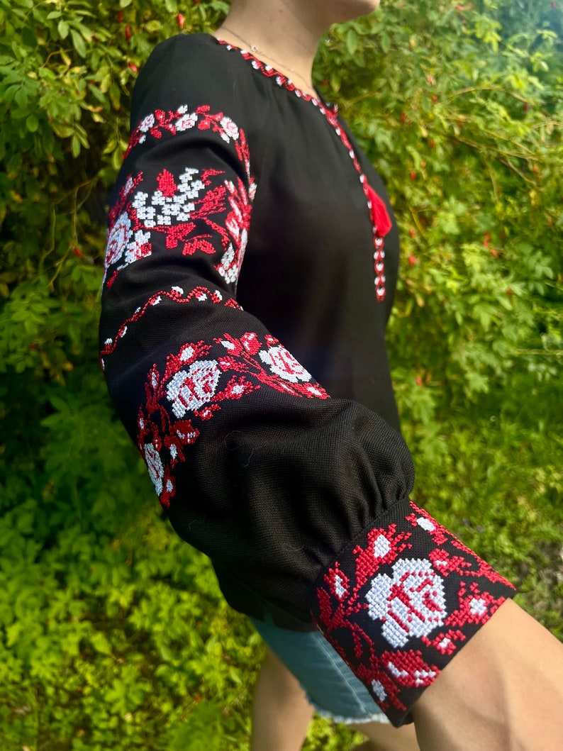 K&ouml;nnte beinhalten: Ein schwarzes Langarmhemd mit roten und wei&szlig;en gestickten Blumendesigns an den &Auml;rmeln und Manschetten.