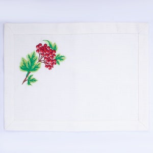 May include: White rectangular placemat with a detailed embroidered design. The embroidery features a cluster of red berries, green leaves, and a brown stem. The placemat has a simple border.
