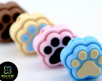 May include: Four colorful paw print shaped silicone charms in brown, beige, pink, and blue. The charms are arranged in a row from left to right.