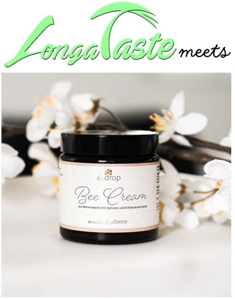 May include: A jar of "Bee Cream" with a black lid and a white label, set against a backdrop of white flowers. The label includes the text "Longa Taste meets" and "Bee Cream" with additional text in German.